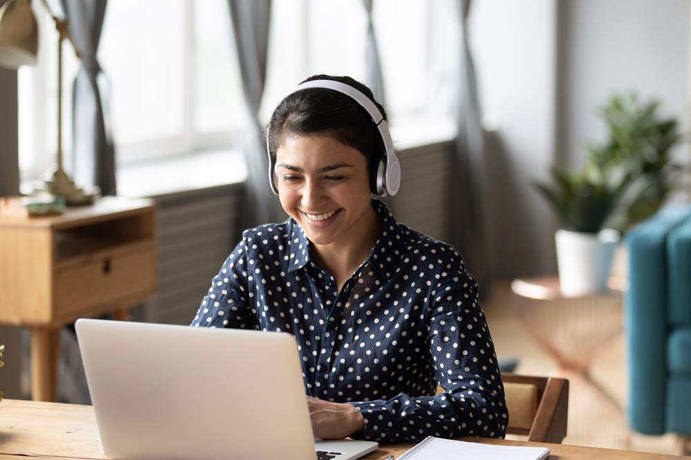 Woman wearing headphones smiles at the laptop she's working on