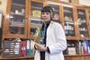 Skye Jenkins wearing a lab coat in a school science prep room she is holding a large beaker with a cactus in and behind her are shelves and of science equipment and chemicals