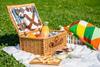 Wicker picnic basket filled with cutlery, plates, food and an orange juice bottle 