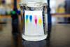 An image showing a beaker containing a thin layer chromatography plate with colourful spots on it