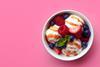 A bowl of vanilla ice cream with raspberries, strawberries and blueberries on a pink background 
