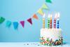 A birthday cake, with five candles, against a light blue background with rainbow coloured bunting.