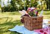 Wicker picnic basket with flowers, baguettes and bottles of drinks on a sunny lawn