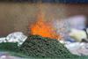 A close-up photograph of a small heap of ammonium dichromate which has been ignited, producing orange sparks and green chromium oxide