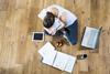 An image from above showing a girl sat cross legged, revising for exams, surrounded by a laptop, tablet, notes, coffee and snack