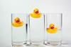 Three rubber ducks floating in three glasses of water.