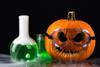 Photograph of Halloween pumpkin wearing lab goggles with scary face and laboratory glassware and mist in black background