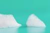 Two clusters of white soap or detergent bubbles on a flat surface against a turquoise background