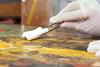 Close of gloved hands cleaning an old painting