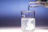 A photo of a test tube of liquid being poured into a beaker of another liquid and a white precipitate forming