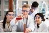 Four high school students in a practical chemistry lesson wearing goggles and lab coats