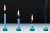 An image showing four stripey blue and white candles, all alight, from left to right, they show the progression of burning