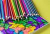 A rainbow selections of crayons stacked on a colourful pattered page of a notepad