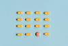 A photograph of yellow-orange pills arranged in rows on a blue background; in the bottom row, a different, red pill stands out