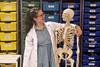 Rebecca Watkins wearing a lab coat with her arm around a teaching skeleton in a science technician's prep room