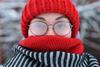 A woman wrapped up in a wooly hat and scarf with fogged up glasses