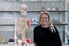 Eleanor Mortimer with a full size model skeleton which has its arm draped casually around her shoulders. They are in a science prep room in front of shelves of glass lab ware.
