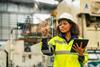An engineer wearing safety gear in an industrial setting interacts with a futuristic screen