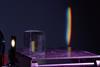 A photograph of a prism on a metal surface as it refracts light from a light source to produce a colour spectrum