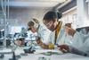 School science laboratory with students lined up along the bench looking at circuitry and microscopes