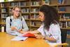 A young woman tutoring a high school student in a school library