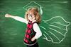 Small girl wearing glasses with arm outstretched in front of a blackboard, where a mortar board and academic cape are drawn