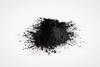A small heap of black activated charcoal against a plain white-grey background