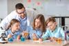 Teacher leaning over three learners who are pouring liquids into chemistry glassware.