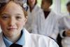 Young girl in lab coat with goggles and three other blurred people in the backgroung
