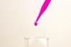 pink drop of liquid falling from pipette into flask