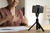 A woman recording herself explaining something on a mobile phone that's sitting on a tripod