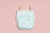 picture of a reusable cloth nappy on a washing line with a pink background