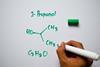 A hand drawing the structure of propanol on a whiteboard