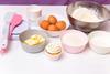 A finished cupcake with the ingredients and tools to make cupcakes including eggs, butter flour, sugar, scales, bowls, paper cups and spatulars