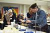 Two teachers in a school lab adjust a plastic pipette in a clamp and stand over a small plastic cup in a microscale experiment set up.