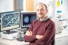 Szabolcs Pap is smiling in front of a computer in a lab.