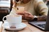 A woman with a tattoo on her arm typing on her mobile phone with a coffee and a chocolate