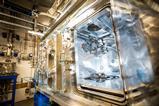 A technician in a white cleansuit makes adjustments inside a large piece of metal scientific equipment