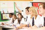 students in a classroom smiling and raising hands
