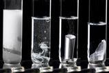 Four test tubes in a row with metals reacting in a clear liquid increasing in bubbles from left to right