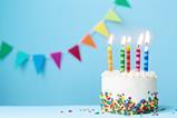 A birthday cake, with five candles, against a light blue background with rainbow coloured bunting.