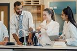 Two students talk to their teacher in a school laboratory while conducting an experiment using a pear-shaped flask