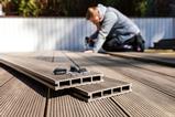 A man uses an electric drill and composite materials to make a decking area in a garden