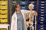 Rebecca Watkins wearing a lab coat with her arm around a teaching skeleton in a science technician's prep room