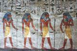 An ancient Egyptian painting on a wall showing hieroglyphics and four standing figures with blue hair