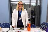 Lynsey Findlay wearing a lab coat manning the science club table at a school fair