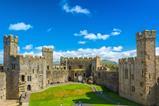 An image of Caernarfon castle with a blue sky and green grass in the castle grounds