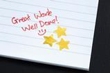 An exercise book with three gold stars and a "great work well done" written in red pen