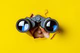 Someone with a pair of binoculars bursting through a wall of yellow paper
