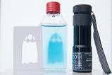 A torch, a stencil of a ghost and a glass bottle with a clear liquid that has the shape of a blue ghost within the liquid